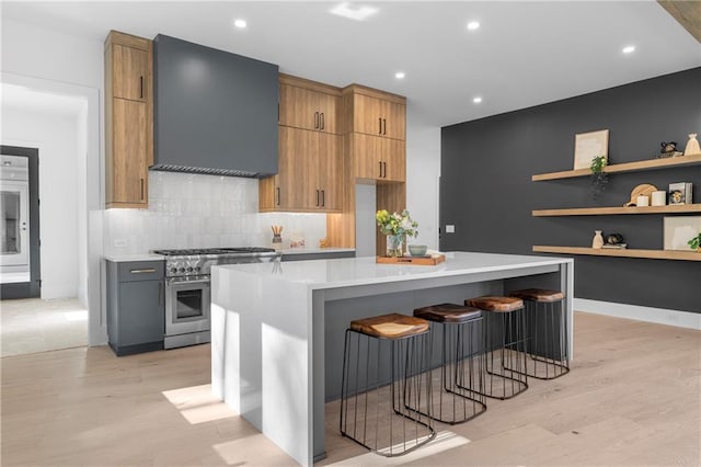 kitchen with backsplash, a kitchen breakfast bar, stainless steel range, a kitchen island, and wall chimney exhaust hood