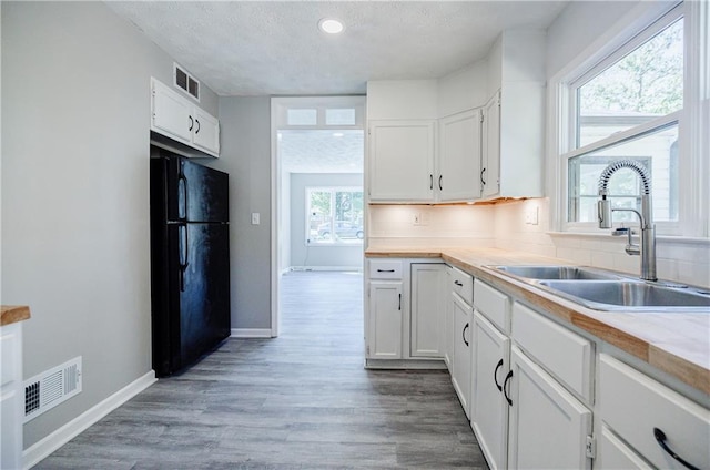 kitchen with sink, white cabinetry, tasteful backsplash, wood-type flooring, and black refrigerator