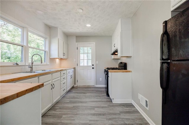 kitchen with white cabinetry, sink, light hardwood / wood-style floors, black appliances, and a textured ceiling