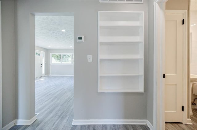 hall with built in shelves, a textured ceiling, and light hardwood / wood-style floors