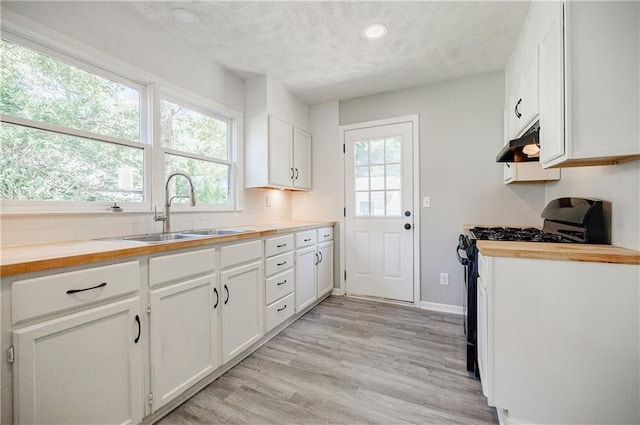 kitchen featuring black gas range, sink, wooden counters, and white cabinets