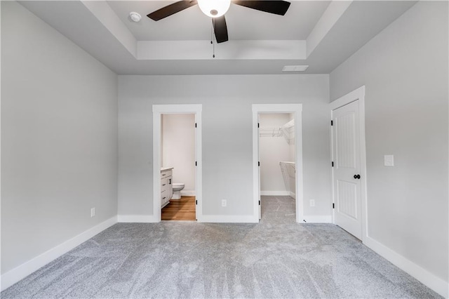 unfurnished bedroom featuring a walk in closet, a tray ceiling, ceiling fan, connected bathroom, and a closet