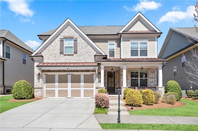 craftsman-style house with covered porch, a standing seam roof, an attached garage, driveway, and brick siding