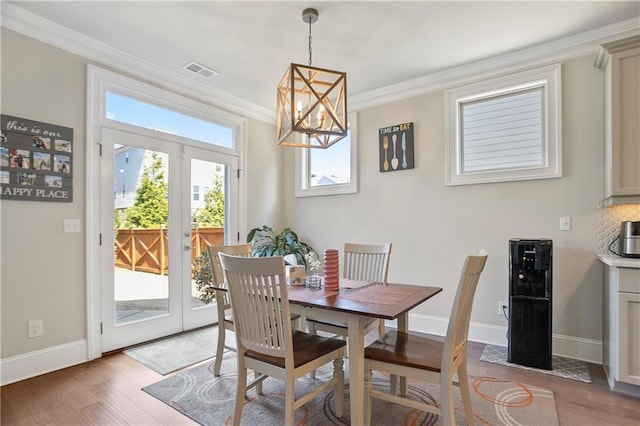 dining space featuring wood finished floors, ornamental molding, a chandelier, baseboards, and french doors
