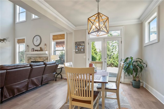 dining room featuring a chandelier, light wood-style floors, a fireplace, baseboards, and ornamental molding