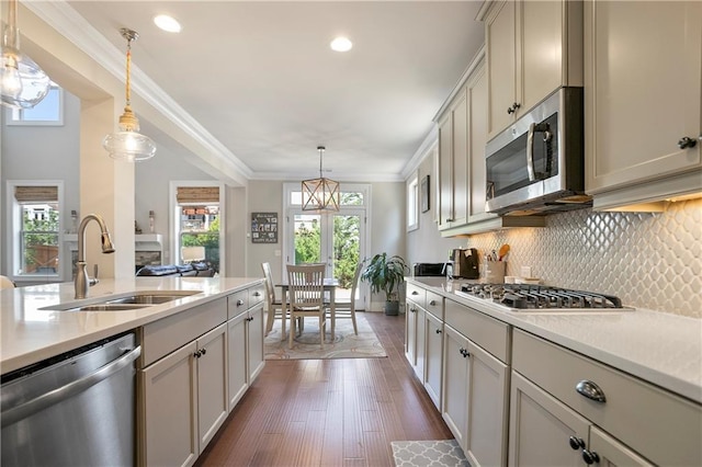 kitchen featuring appliances with stainless steel finishes, a sink, light countertops, decorative backsplash, and hanging light fixtures