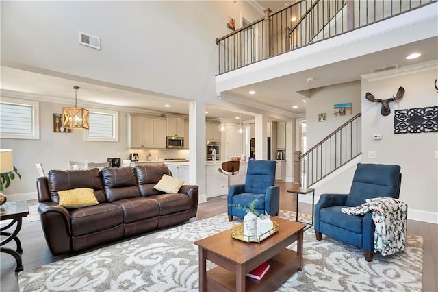living area with light wood-style floors, stairs, a towering ceiling, baseboards, and a chandelier
