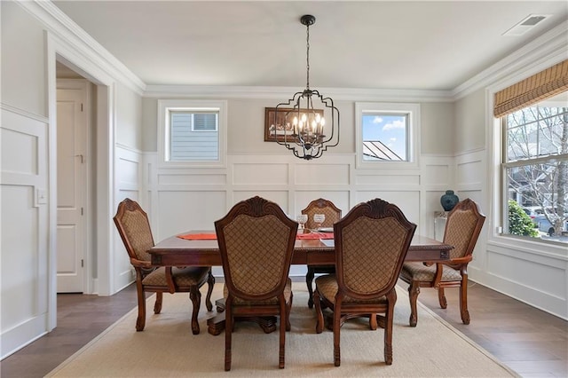 dining room featuring a chandelier, a decorative wall, plenty of natural light, a wainscoted wall, and ornamental molding