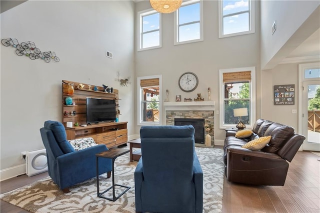 living area featuring plenty of natural light, a high ceiling, a stone fireplace, baseboards, and wood finished floors
