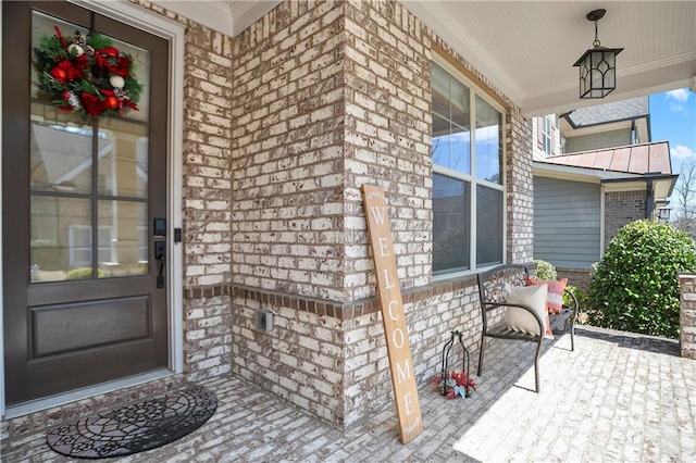 view of exterior entry with brick siding, a standing seam roof, a porch, and metal roof