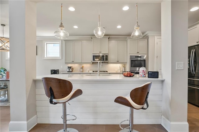 kitchen with appliances with stainless steel finishes, light countertops, backsplash, a breakfast bar area, and baseboards