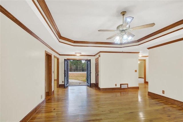 empty room featuring a tray ceiling, visible vents, ornamental molding, wood finished floors, and baseboards