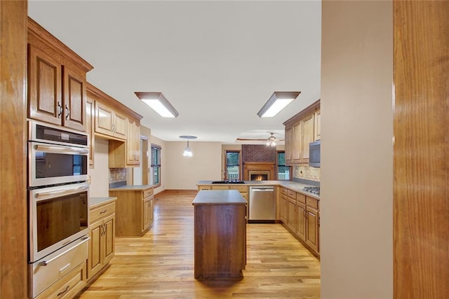 kitchen featuring decorative light fixtures, light wood finished floors, stainless steel appliances, backsplash, and a peninsula