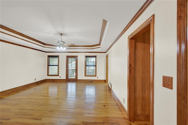 empty room featuring light wood-style floors, a tray ceiling, ornamental molding, and baseboards