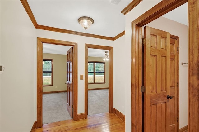 hallway with light wood-style floors, crown molding, and baseboards