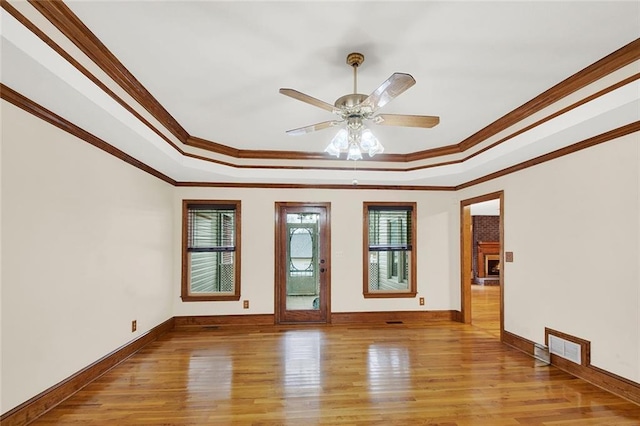 empty room featuring ornamental molding, a raised ceiling, light wood-style flooring, and baseboards