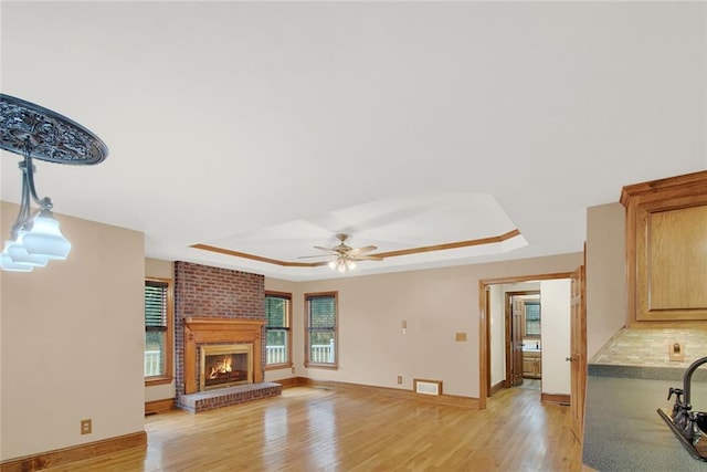 living area with light wood finished floors, a tray ceiling, a fireplace, and a healthy amount of sunlight