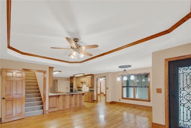 entrance foyer featuring a tray ceiling, light wood finished floors, ceiling fan, baseboards, and stairs