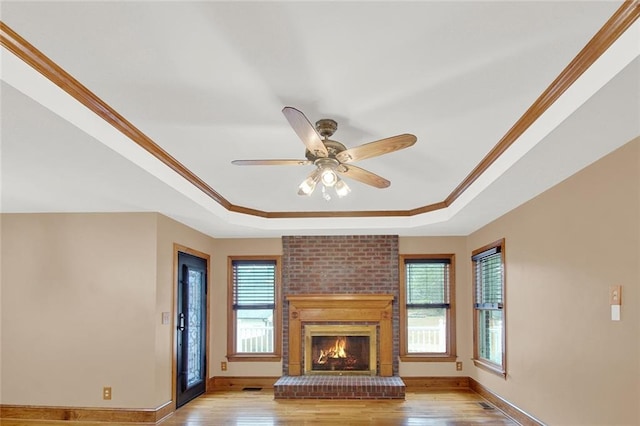 unfurnished living room featuring a fireplace, light wood finished floors, a raised ceiling, ornamental molding, and baseboards