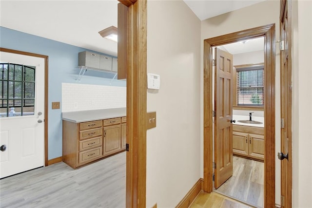 hallway featuring light wood finished floors, baseboards, and a sink