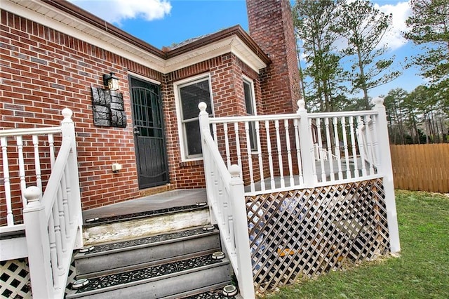 doorway to property with brick siding, a chimney, and fence