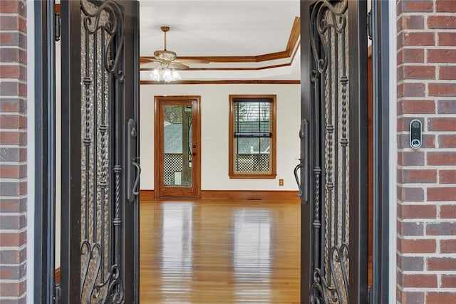 foyer entrance with ceiling fan, light wood-style flooring, brick wall, baseboards, and ornamental molding