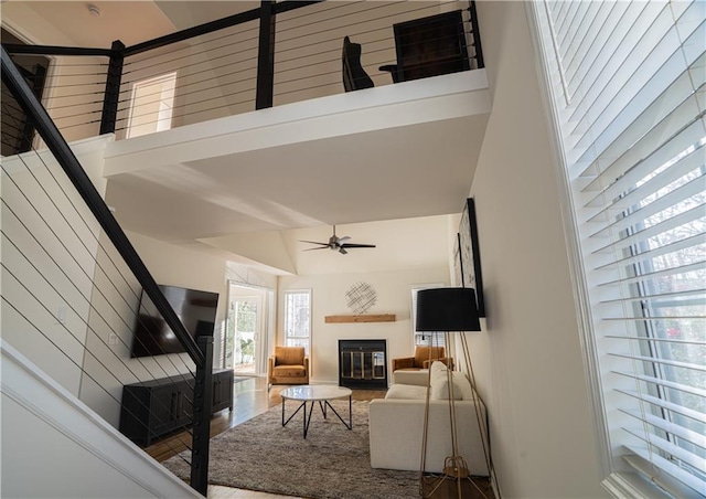 living area featuring a glass covered fireplace, ceiling fan, a towering ceiling, and stairs