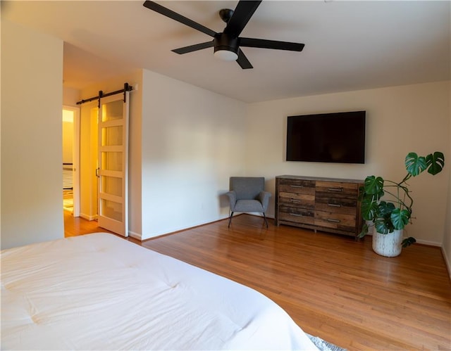 bedroom with ceiling fan, a barn door, wood finished floors, and baseboards