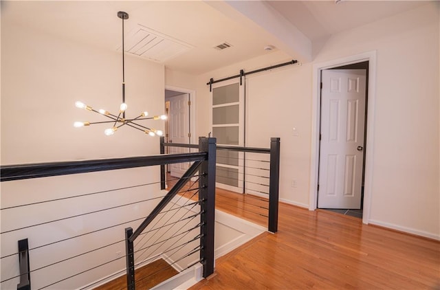 hallway with a barn door, light wood-style flooring, a notable chandelier, visible vents, and an upstairs landing