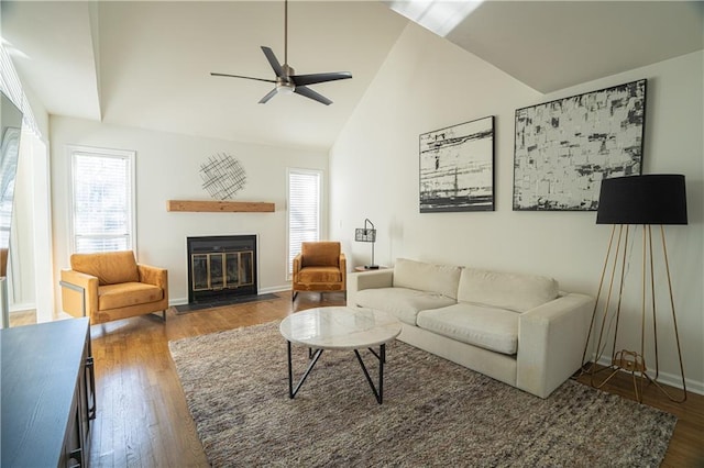 living room featuring baseboards, a ceiling fan, lofted ceiling, a fireplace with flush hearth, and wood finished floors