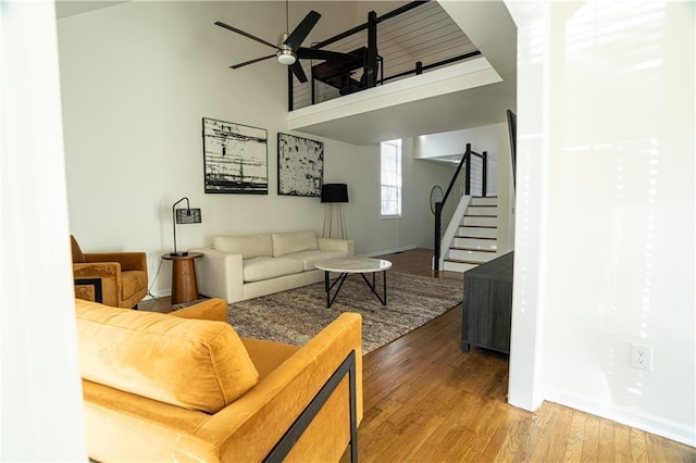 living room with a towering ceiling, ceiling fan, wood finished floors, baseboards, and stairs