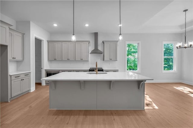 kitchen featuring wall chimney range hood, gray cabinetry, light countertops, and recessed lighting