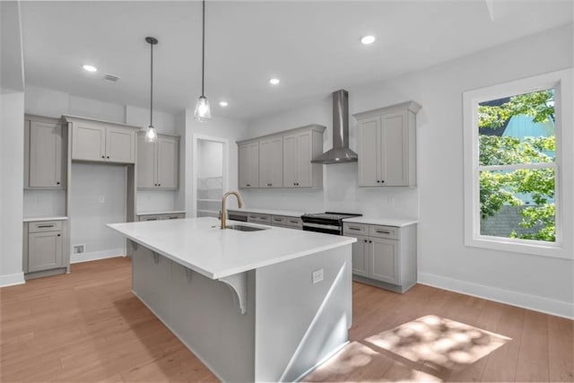kitchen featuring wall chimney range hood, gray cabinets, a sink, baseboards, and recessed lighting