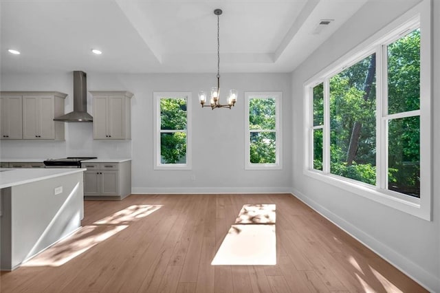 kitchen with wall chimney exhaust hood, baseboards, light countertops, hanging light fixtures, and light wood-type flooring