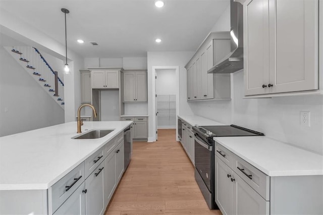 kitchen featuring range with electric stovetop, a sink, wall chimney range hood, light wood-type flooring, and recessed lighting