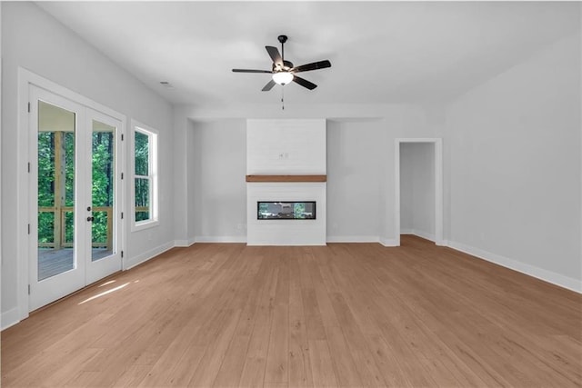 unfurnished living room featuring ceiling fan, baseboards, light wood-style flooring, and a glass covered fireplace