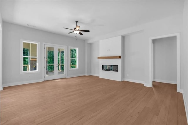 unfurnished living room with a ceiling fan, baseboards, a glass covered fireplace, light wood-style floors, and french doors