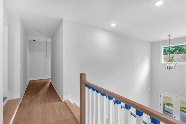 hallway with an upstairs landing, light wood finished floors, a chandelier, baseboards, and recessed lighting