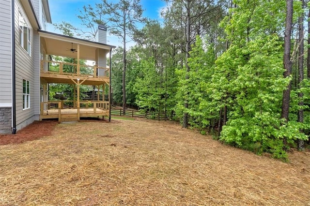 view of yard featuring a wooden deck, ceiling fan, a balcony, and fence