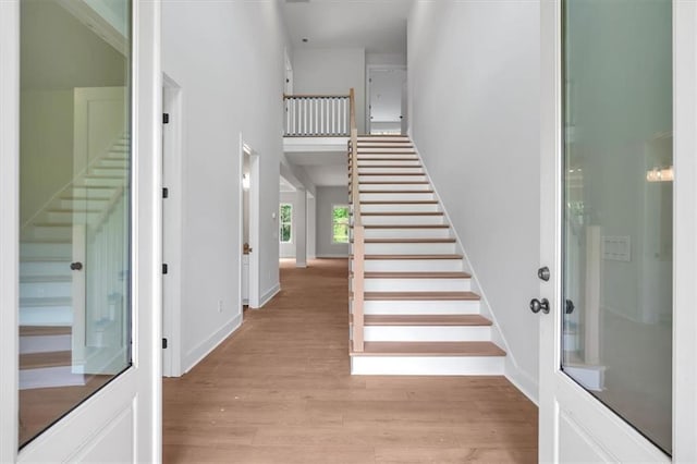 staircase featuring wood finished floors, a high ceiling, and baseboards