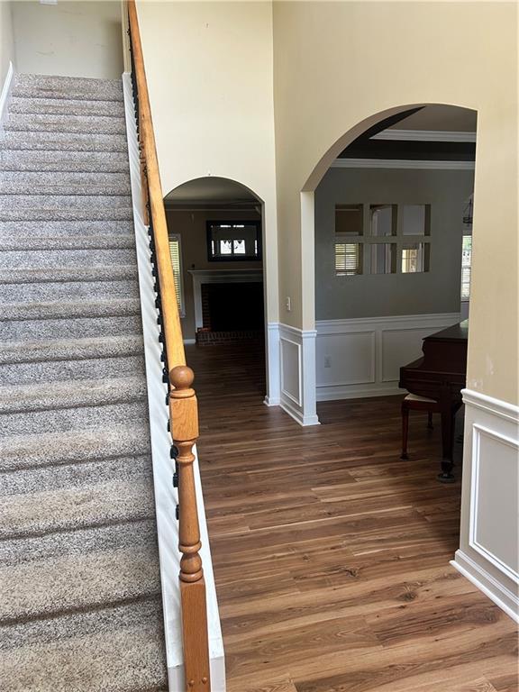 1038 Island View Ct, Buford, GA 30518 - stairs featuring crown molding, wood finished floors, arched walkways, wainscoting, and a decorative wall