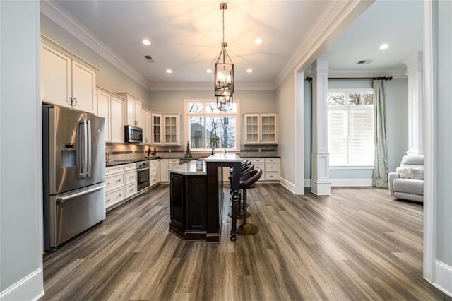 kitchen with stainless steel appliances, a center island, a kitchen bar, decorative light fixtures, and ornate columns