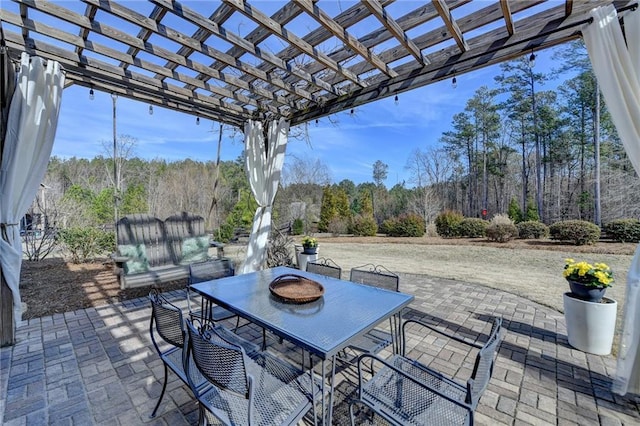 view of patio / terrace featuring a wooded view, outdoor dining area, and a pergola