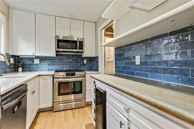 kitchen featuring sink, backsplash, light hardwood / wood-style floors, white cabinets, and appliances with stainless steel finishes