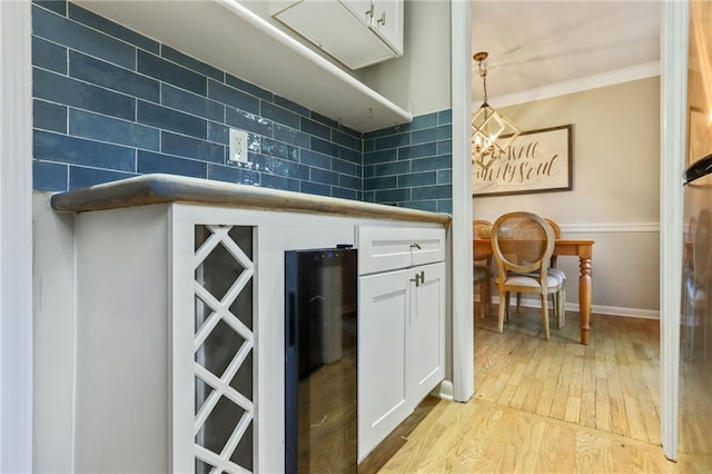 interior space featuring decorative backsplash, crown molding, light hardwood / wood-style floors, white cabinetry, and hanging light fixtures