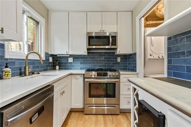 kitchen featuring stacked washing maching and dryer, white cabinetry, sink, and appliances with stainless steel finishes