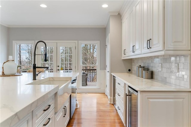 kitchen with ornamental molding, light wood-type flooring, beverage cooler, and plenty of natural light