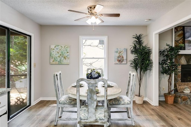 dining area with light hardwood / wood-style flooring, ceiling fan, a fireplace, and a textured ceiling