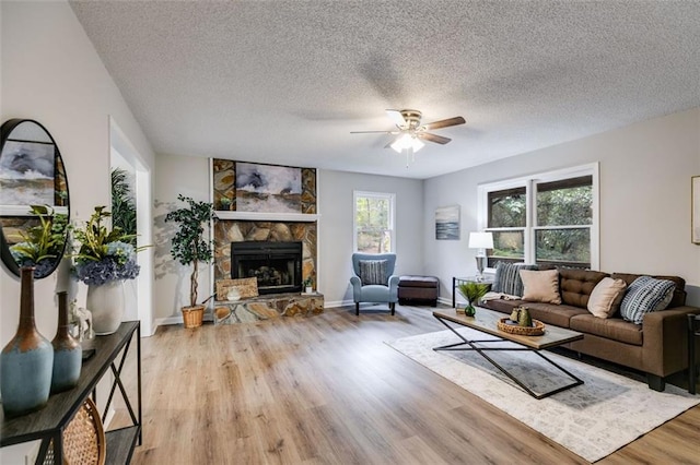 living room with a textured ceiling, a fireplace, ceiling fan, and light wood-type flooring