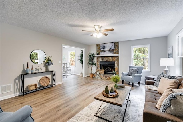 living room featuring ceiling fan, a textured ceiling, a fireplace, and light wood-type flooring